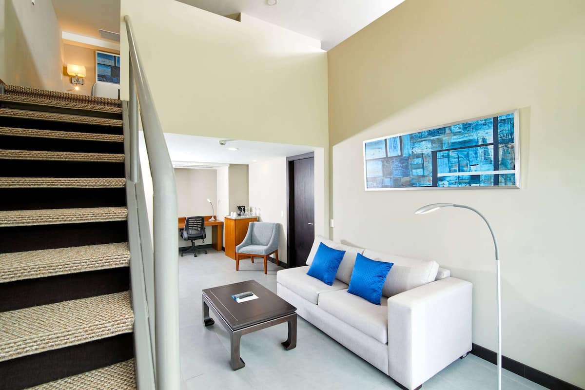 Un salon moderne avec un escalier, un canapé agrémenté de coussins bleus, une table basse et un tableau accroché au mur.