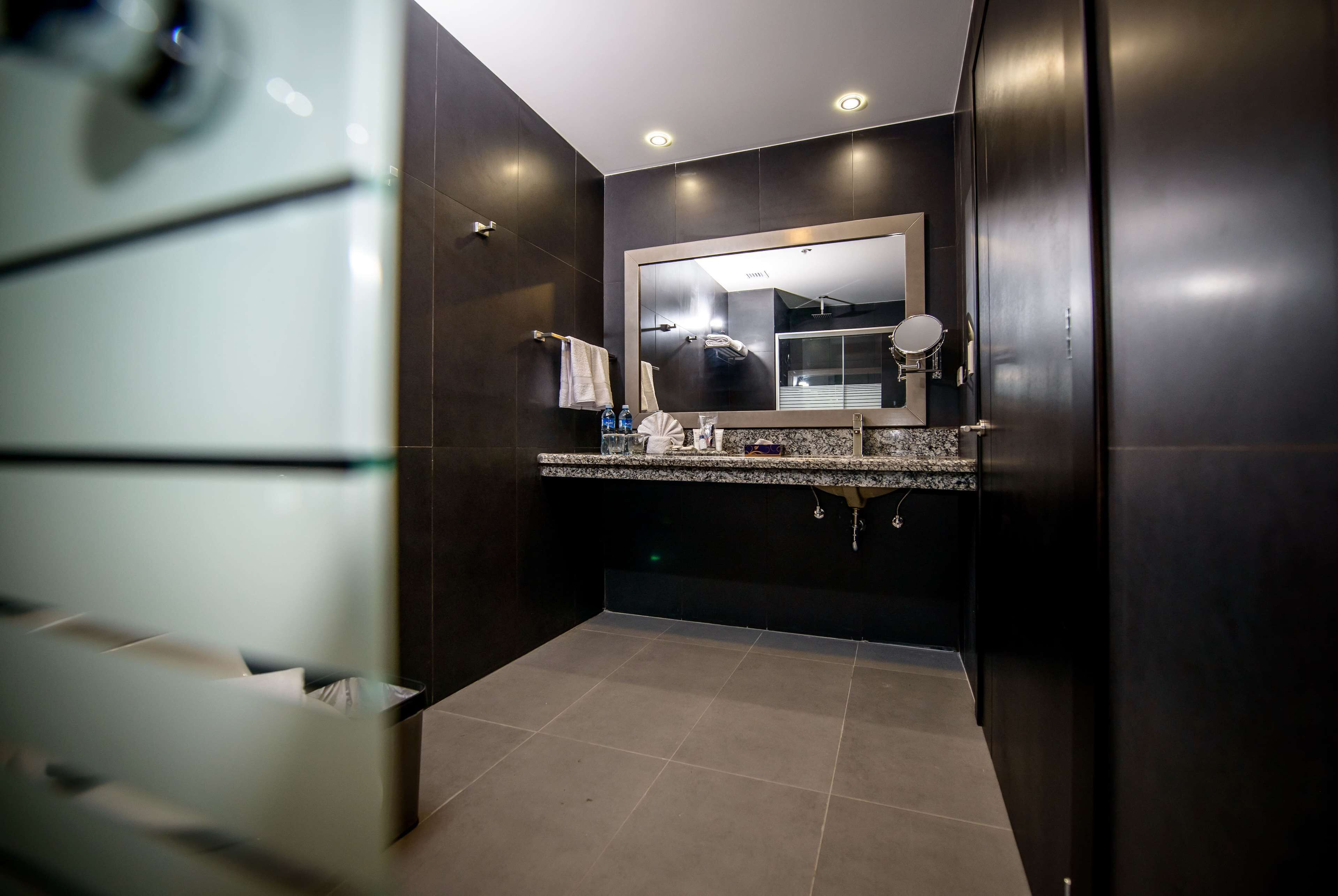 A modern bathroom with dark walls, a large mirror, and a granite countertop.