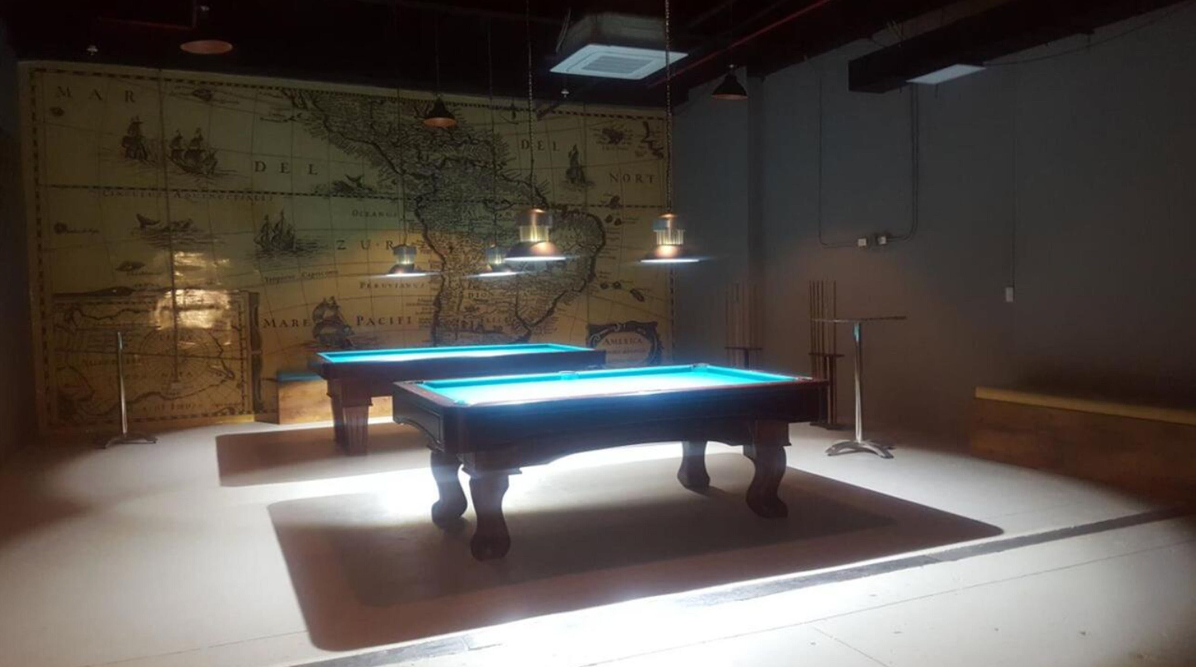 Two pool tables in a dimly lit room with a large map on the wall.