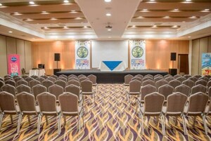 Un salón de conferencias con hileras de sillas orientadas hacia un escenario, una alfombra estampada e iluminación empotrada en el techo.