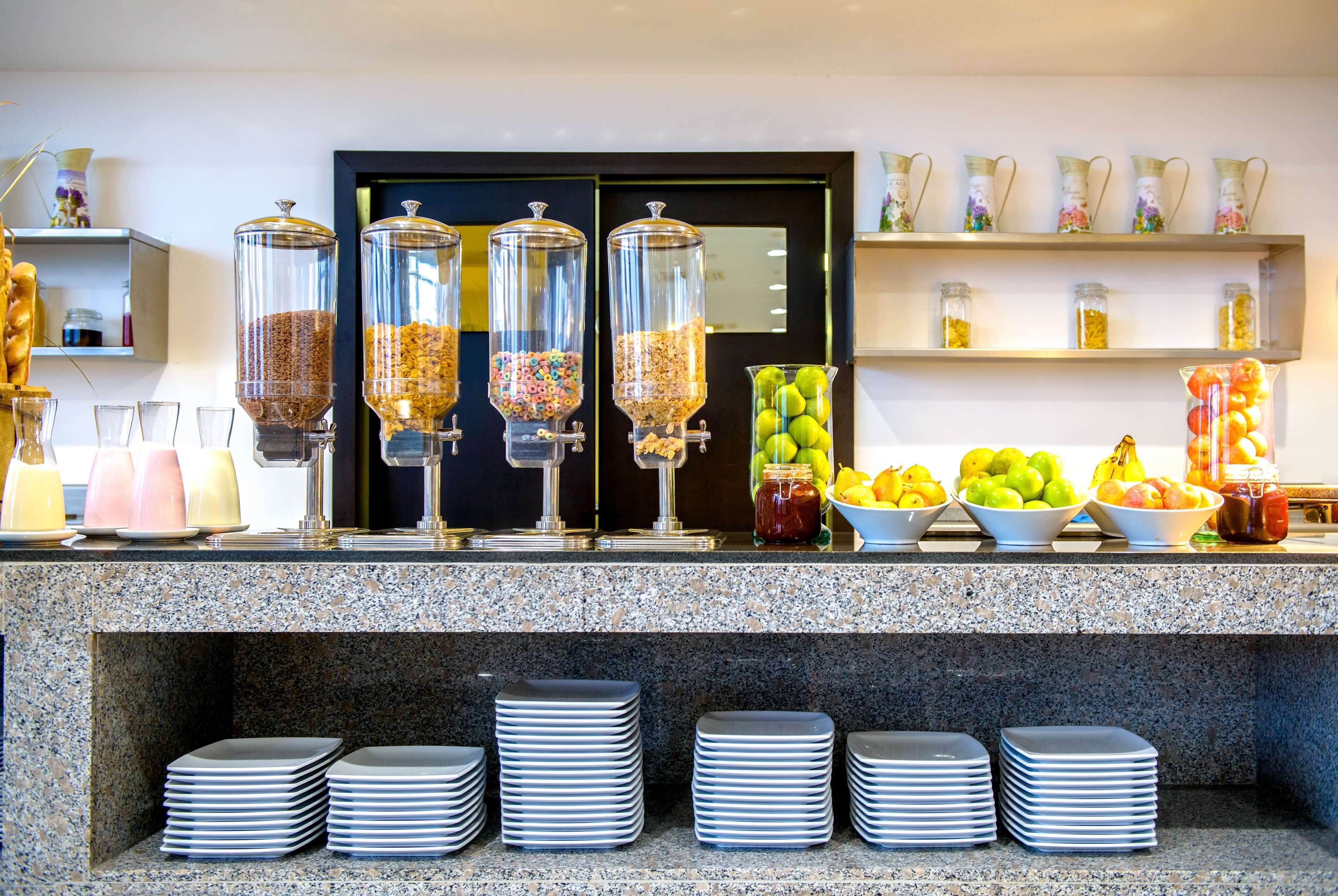 A buffet area with food dispensers, bowls of fruits, and stacked plates.