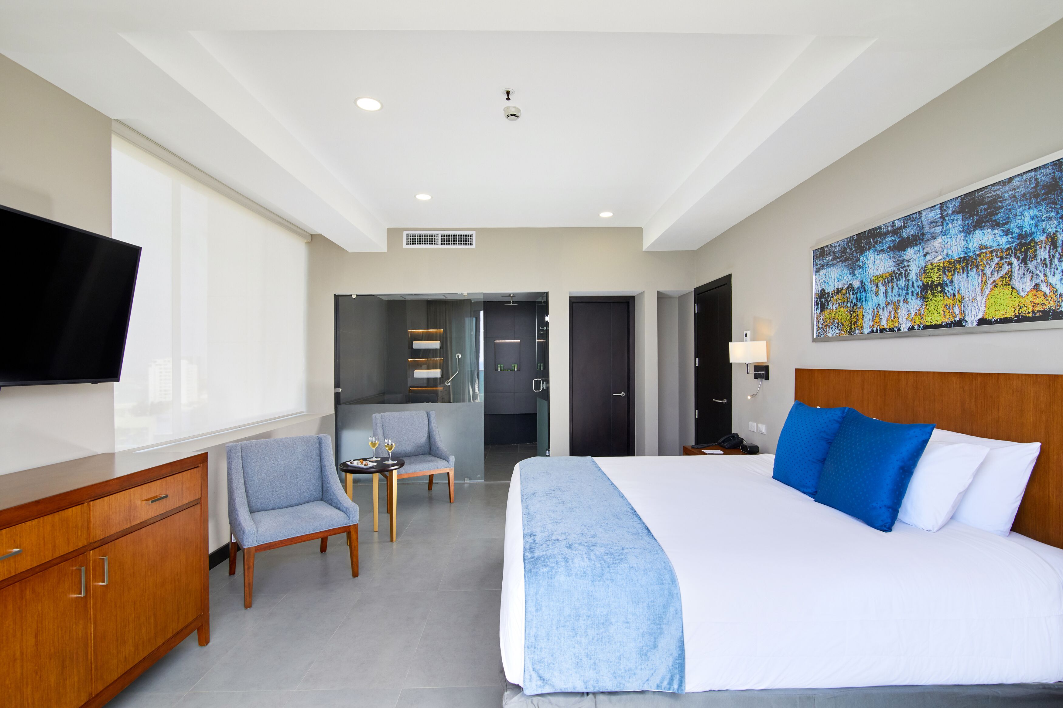 A hotel room with a large bed, a desk with a chair, a TV, and a painting on the wall.