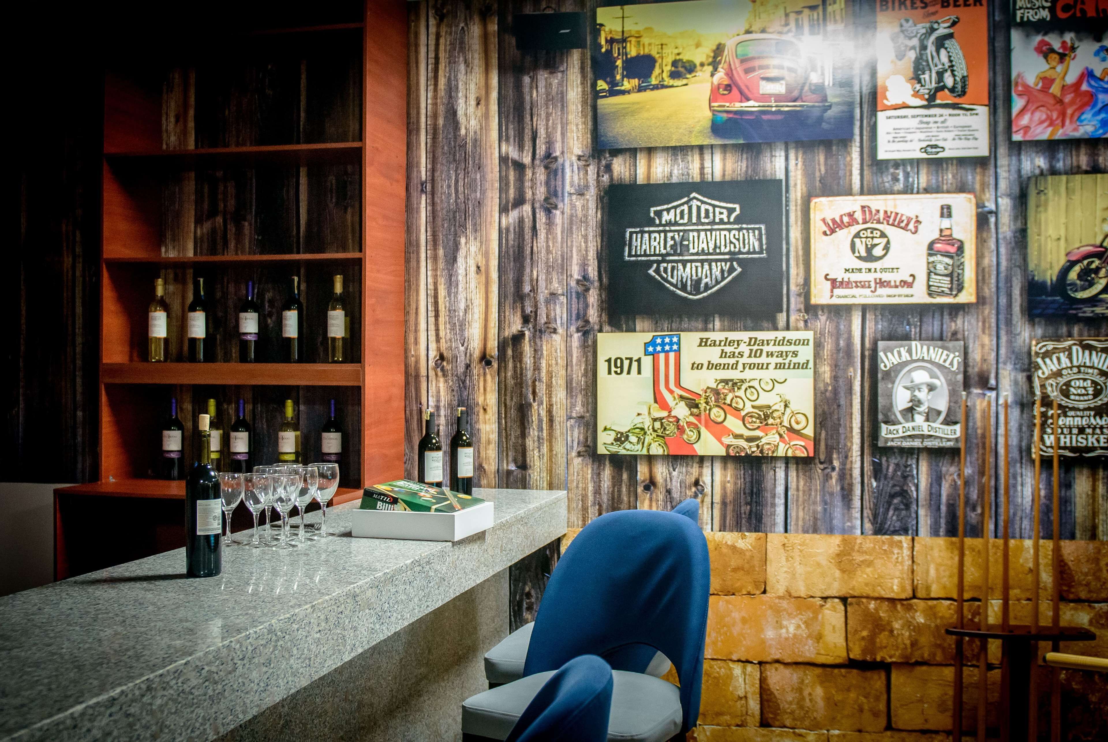 A bar area with a wooden wall, a counter with wine bottles and glasses, and various memorabilia including a Harley-Davidson sign and a Jack Daniel's sign.