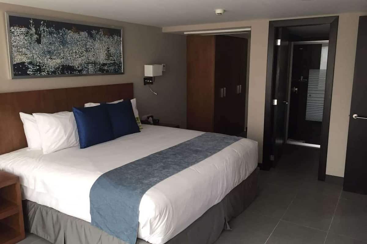 Une chambre d’hôtel avec un grand lit, une table de chevet, une armoire et un tableau au mur.