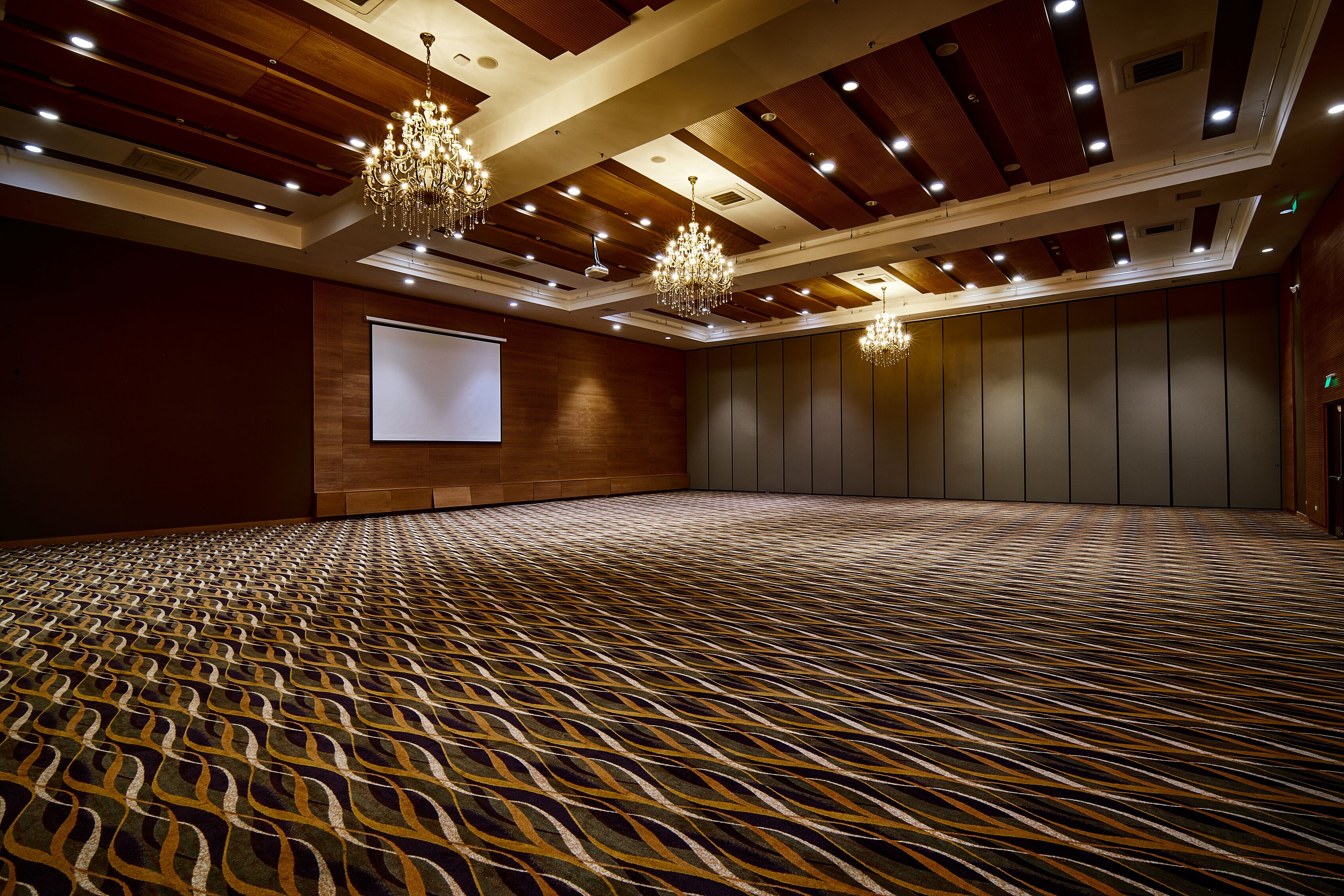 A large conference room with a patterned carpet, wooden ceiling panels, and chandeliers.
