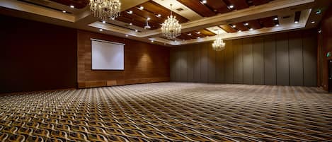 A large conference room with a patterned carpet, wooden ceiling panels, and chandeliers.