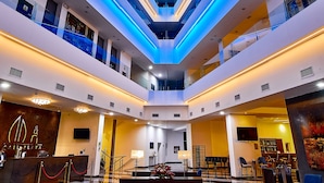 Un moderno vestíbulo de hotel con un área de estar central, varios pisos y un techo con iluminación lineal.