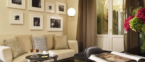 A living room with a sofa, coffee table, and a book on a side table. There are framed pictures on the wall and a vase with flowers on a table.