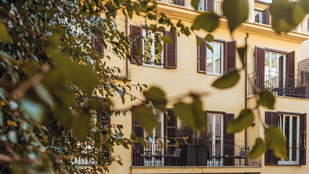 Un immeuble à plusieurs étages doté de balcons, d’un espace extérieur aménagé pour s’asseoir et d’un jardin.