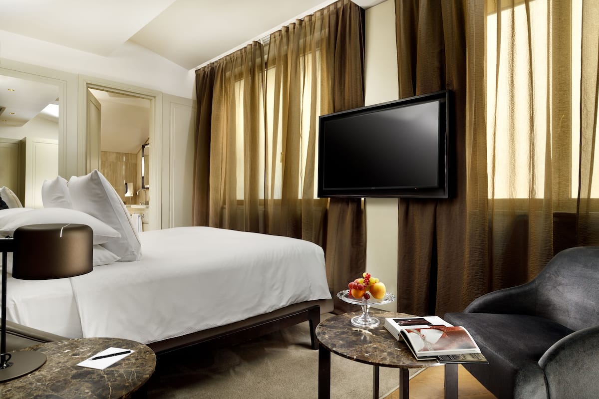 Habitación de hotel con una cama, un televisor de pantalla plana, una mesita de centro con una revista y una silla.
