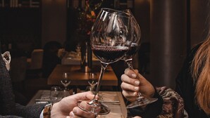 Gros plan de deux personnes tenant des verres à vin autour d’une table dans une pièce à l’éclairage tamisé, dont l’intérieur présente un design moderne.