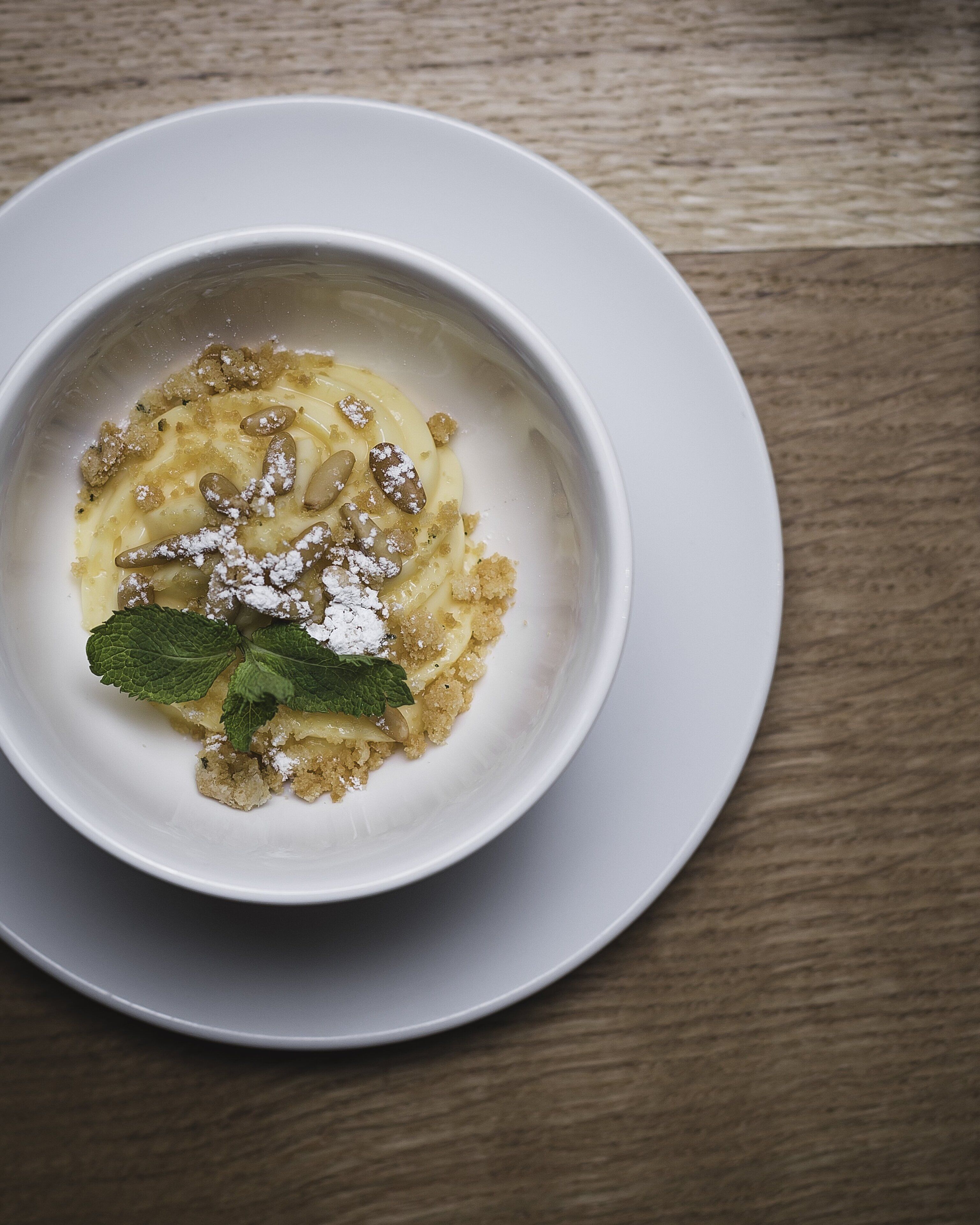 Un tazón blanco de postre sobre un plato blanco, colocado en una mesa de madera.