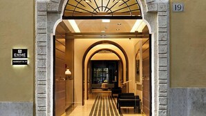 Entrada de hotel con un arco de piedra, un cartel que indica la habitación número 19 y una zona de recepción con una lámpara y asientos.