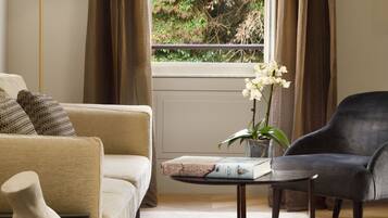 Una sala de estar moderna con un sofá, una mesa de centro, un sillón y vistas a zonas verdes por una ventana.