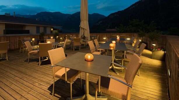 An outdoor dining area with tables and chairs, an umbrella, and a mountainous backdrop. - Hotel Weiss Kreuz (Thusis)