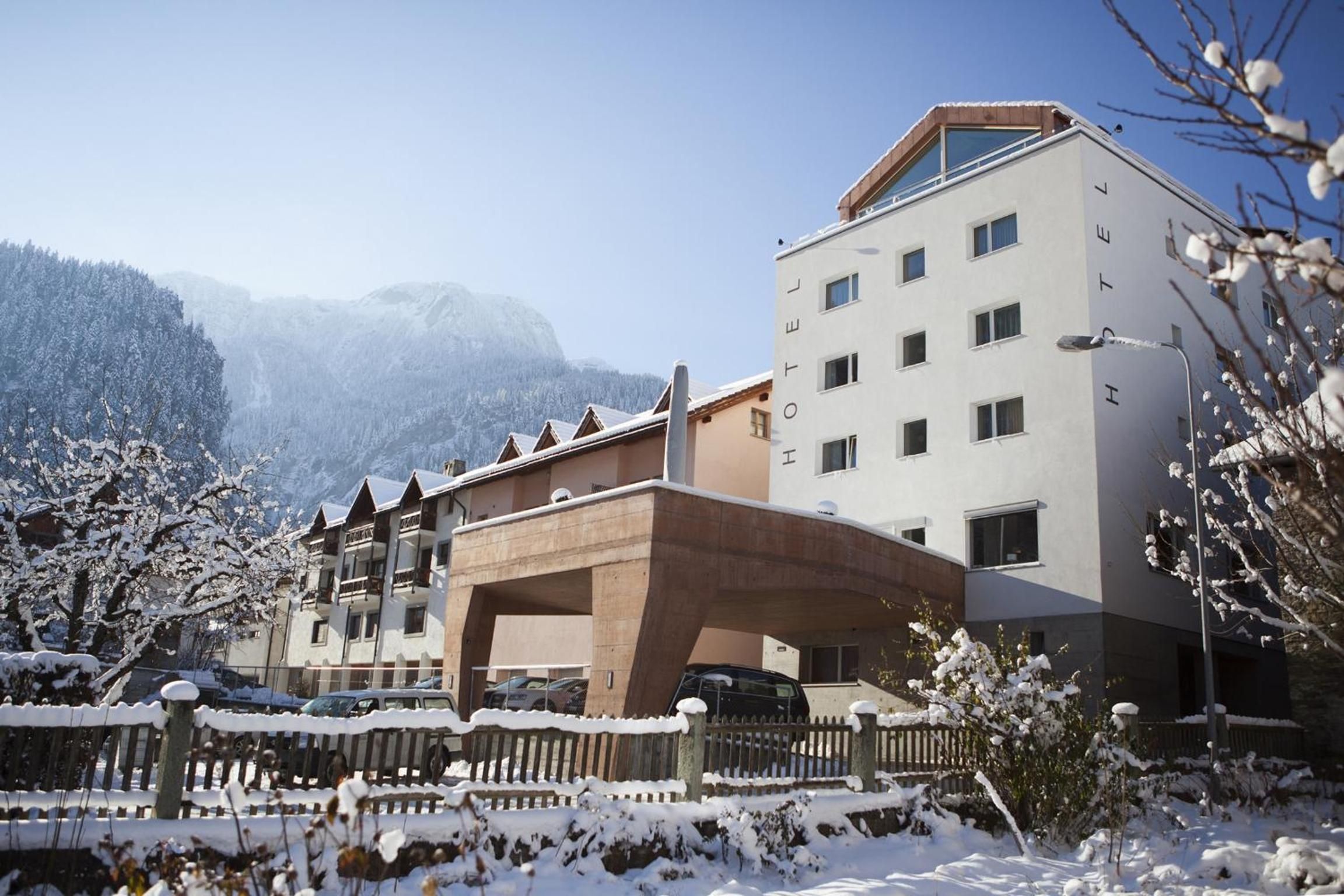 Ein Hotel mit modernem Design, das einen markanten Eingangsbereich und einen Blick auf verschneite Berge im Hintergrund bietet.