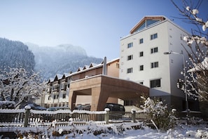 Un hotel de diseño moderno, con una entrada destacada y vistas a montañas nevadas al fondo.