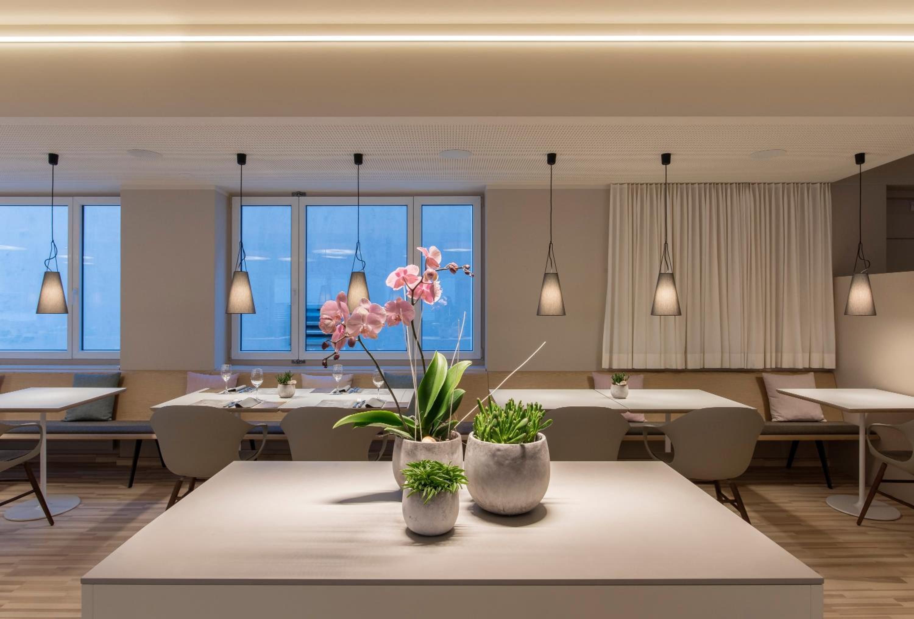Un espace de restauration moderne, avec des tables, des chaises et des luminaires suspendus.
