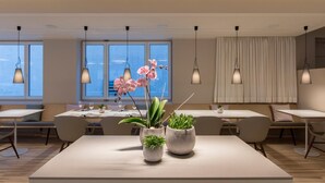 A modern dining area with tables, chairs, and hanging pendant lights. - Hotel Weiss Kreuz (Thusis)