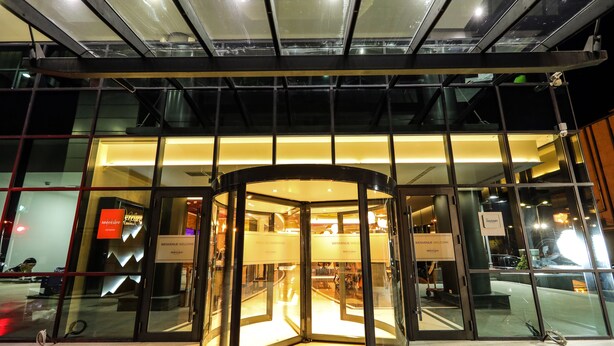 Une porte tournante donne accès à un bâtiment dont la façade est constituée de panneaux de verre et sur laquelle on peut lire l’inscription « Bienvenue ».
