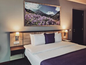 Habitación de hotel con cama, dos lámparas de noche, una mesita de noche, un cuadro colgado en la pared y una puerta.