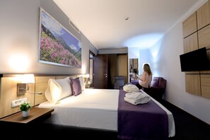 Una habitación de hotel con cama, escritorio, silla, televisor y un cuadro en la pared.