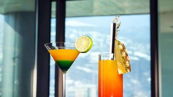Deux cocktails sont posés sur une table, et la vue sur les montagnes est magnifique à travers les grandes fenêtres.