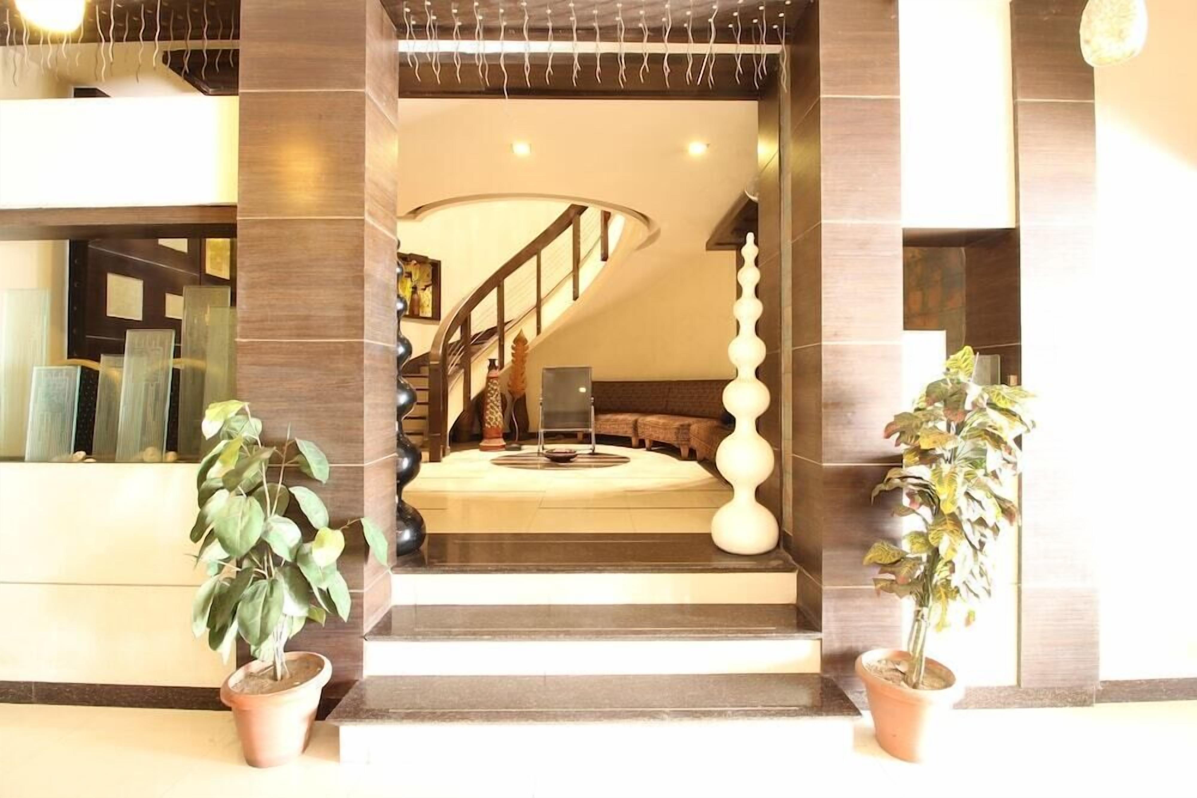 A modern lobby with a staircase leading to a second floor, potted plants, and a reception desk.