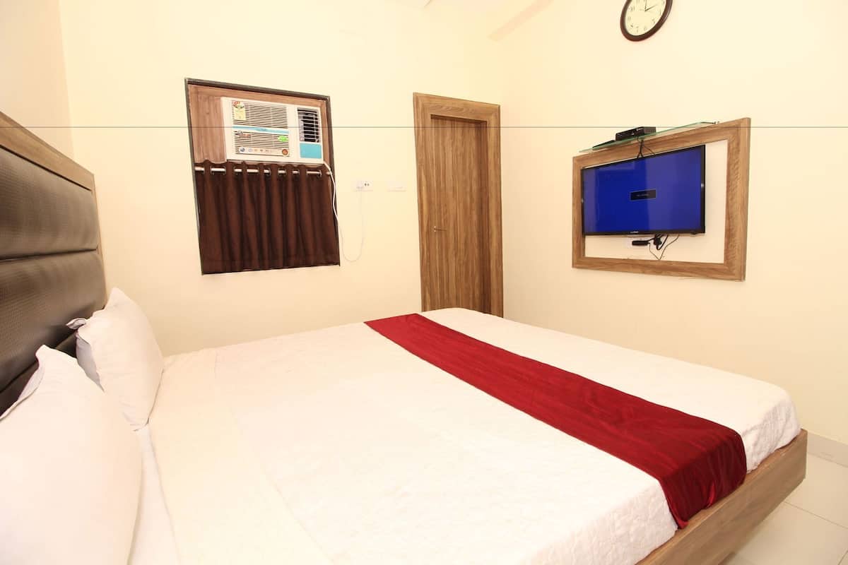 Un dormitorio con cama, televisión montada en la pared, un reloj y una ventana con cortinas.