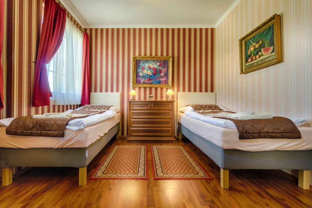 A hotel room with two beds, a dresser, a painting, and a fruit painting on the wall.