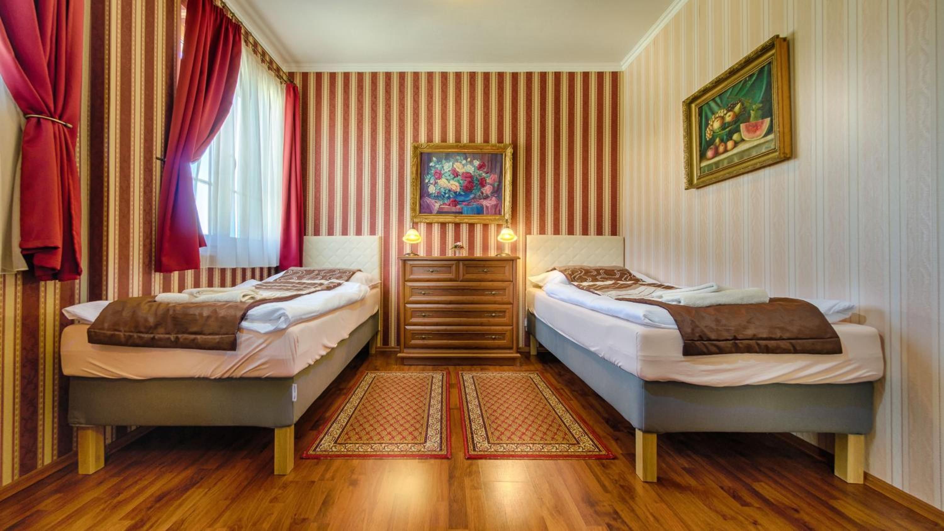 A hotel room with two beds, a dresser, a painting, and a fruit painting on the wall.