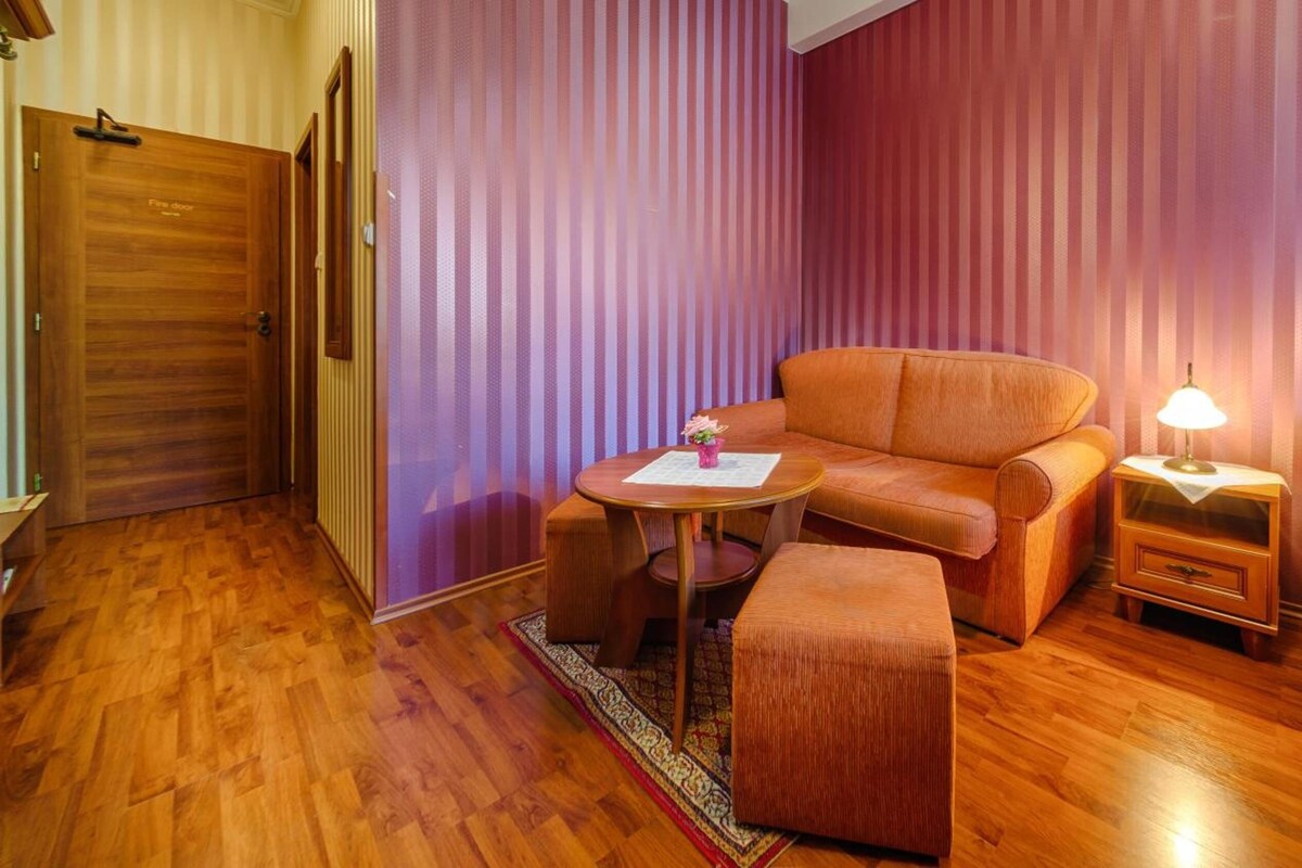 A room with a bed, a sofa, a small table, and a nightstand.