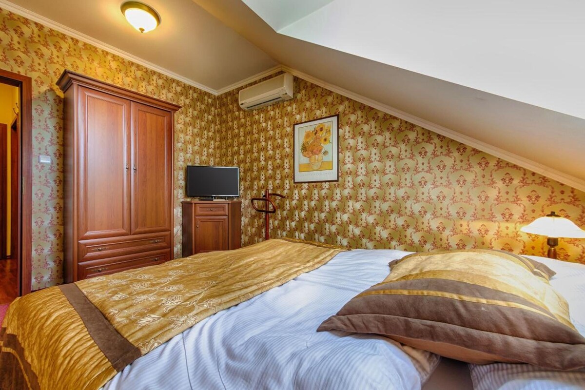 A bedroom with a bed, wardrobe, television, and a painting on the wall.