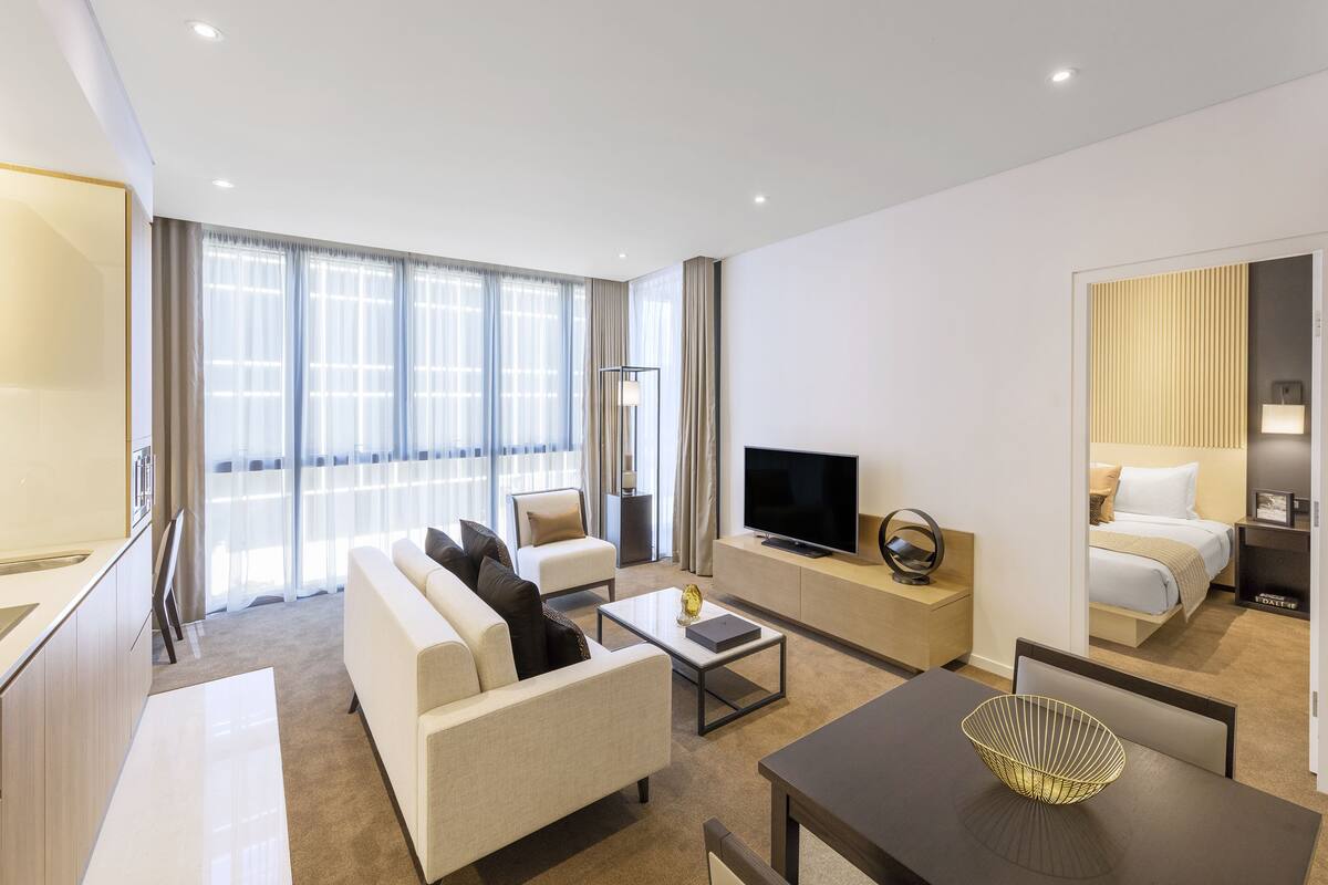 A modern hotel room with a sofa, a coffee table, a TV, a bed, and a dining area.