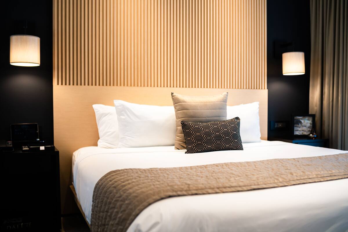 A neatly made bed with white and patterned pillows, a textured blanket, and two bedside tables with lamps.