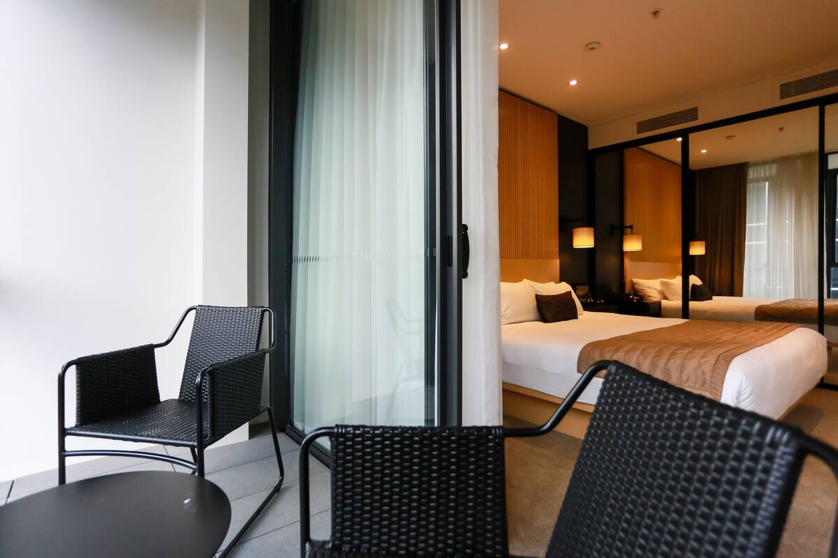A hotel room with a bed, two chairs, a small table, and a sliding glass door leading to a balcony.