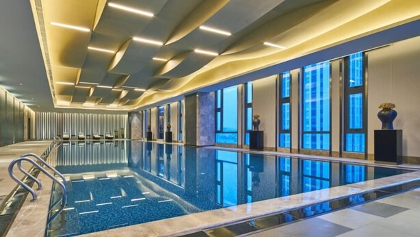 A modern indoor swimming pool with a long, narrow design, surrounded by glass walls and a sleek ceiling with integrated lighting. - Wanda Realm Shangrao (Shangrao)