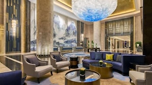 A spacious lobby with a large chandelier, seating area, and a wall with a mountainous painting. - Wanda Realm Shangrao (Shangrao)
