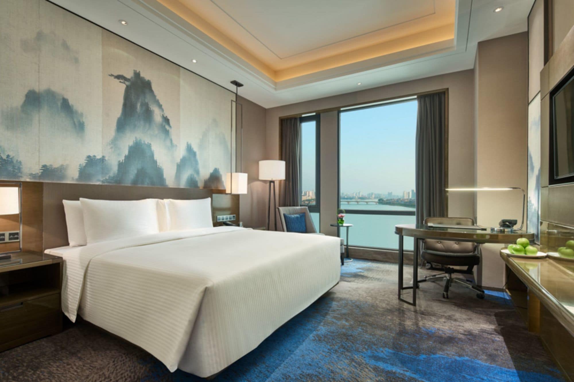 A hotel room with a large bed, a desk, a chair, a TV, and a painting on the wall.