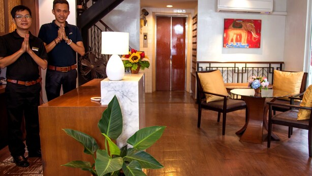 A reception area with a marble counter, a potted plant, a lamp, a sofa, and a painting on the wall. - Tarntawan Place Apartments (Bangkok Noi)