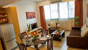 A living room with a dining area, a flat-screen TV, a refrigerator, and a painting on the wall. - Tarntawan Place Apartments (Bangkok Noi)