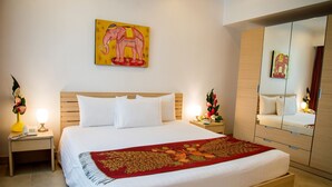 A hotel room with a bed, a nightstand with a lamp, a mirror, and a painting of an elephant on the wall. - Tarntawan Place Apartments (Bangkok Noi)