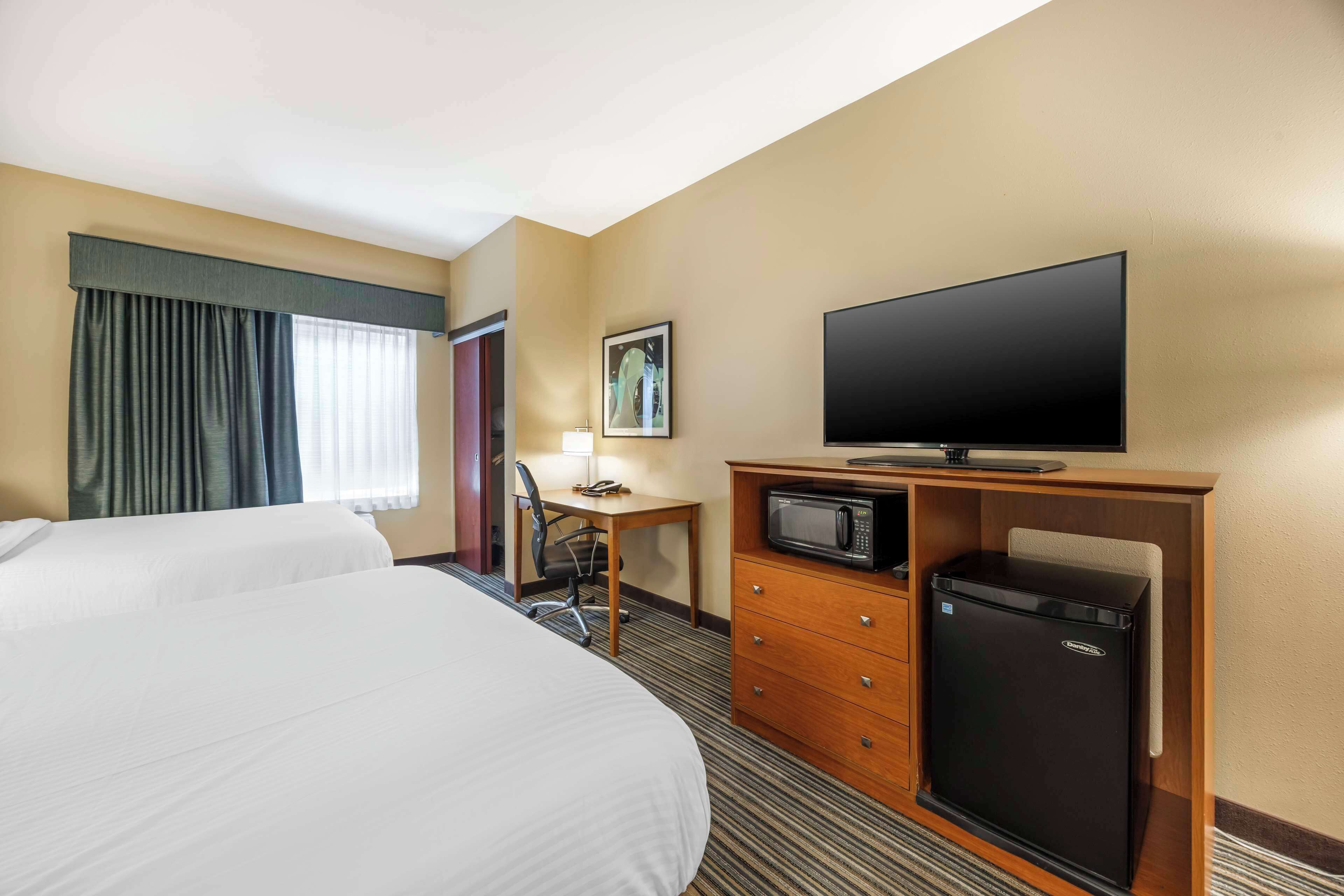 A hotel room with two beds, a desk with a chair, a television, a microwave, and a refrigerator.