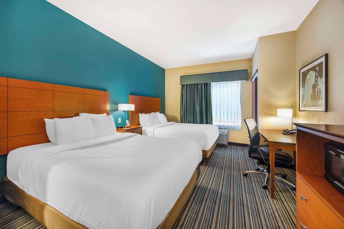 Ein Hotelzimmer mit zwei Betten, einem Schreibtisch, einem Stuhl und einem Fernseher.