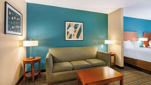 Habitación de hotel con una pared de acento color turquesa, un sofá, una mesa de centro de madera, una cama con ropa blanca y dos lámparas de noche.