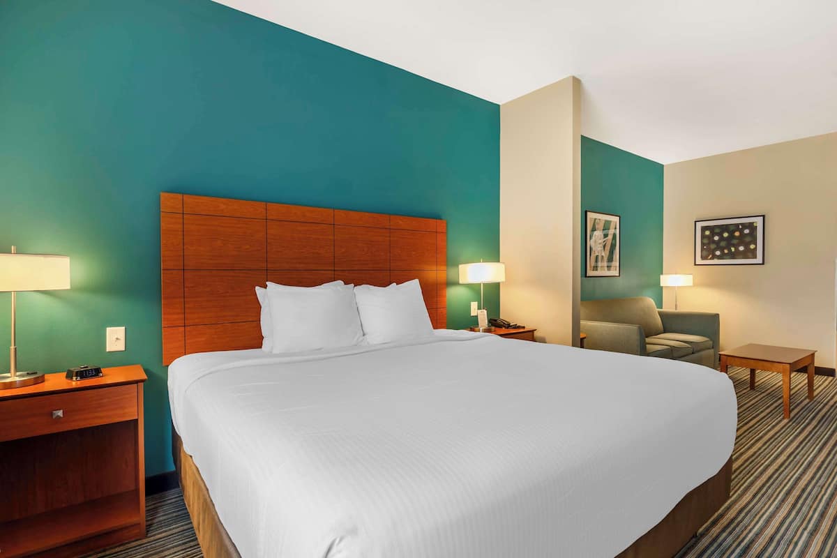 Ein Hotelzimmer mit einem großen Bett, einem Holzkopfschild, zwei Nachttischen mit Lampen, einem Sessel und einem kleinen Tisch.