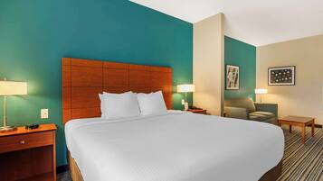A hotel room with a large bed, wooden headboard, two bedside tables with lamps, a chair, and a small table.