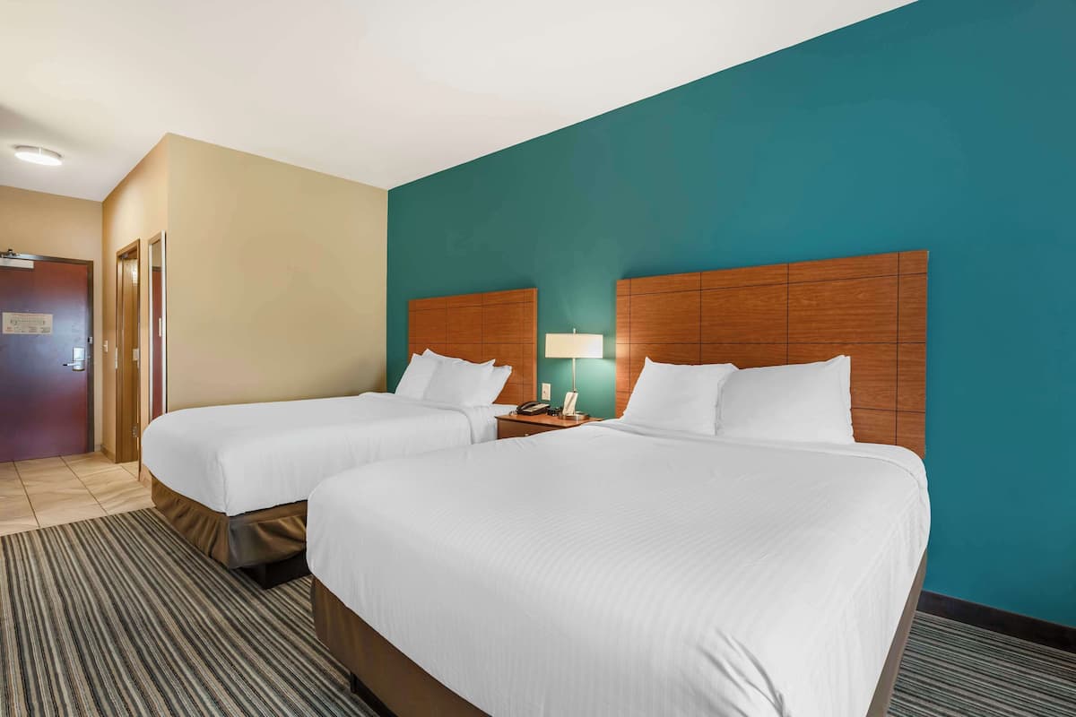 Ein Hotelzimmer mit zwei Betten, einem Holzkopfstück, einem Nachttisch mit Lampe und einer Tür links.