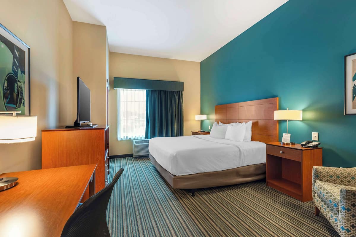 Ein Hotelzimmer mit einem Bett, Nachttischen, einem Schreibtisch, einem Sessel und einem Fernseher.