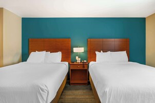 Una habitación de hotel con dos camas, una mesita de noche con lámpara y un cabecero de madera.